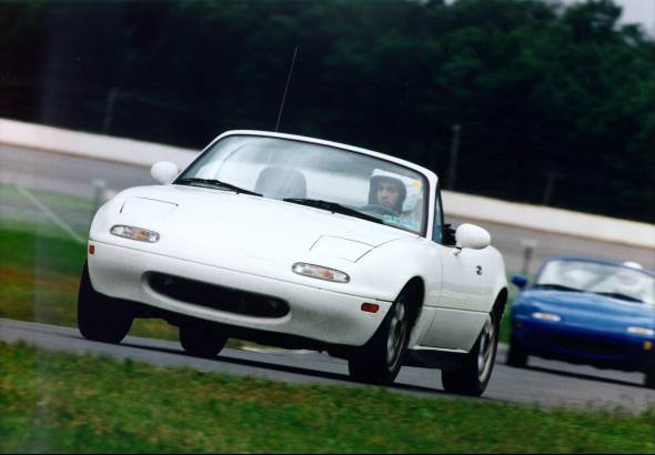 A white Miata with a blue Miata
 following it